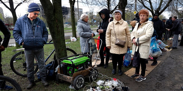 Local residents gather near a generator to charge their mobile devices in an area controlled by Russian-backed separatist forces in Mariupol, Ukraine, Friday, April 22, 2022 (AP Photo/Alexei Alexandrov)