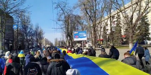 Live broadcast footage shows people holding a banner in the colors of the Ukrainian flag as they protest against Russia's invasion of Ukraine, in Kherson, Ukraine, on March 13, 2022, in this still image from a social media video obtained by Reuters.