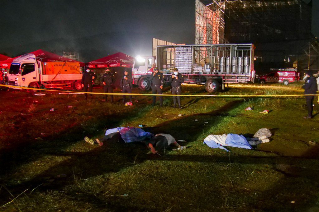 Firefighters and police stand next to the bodies of people who died in a stampede during an outdoor concert to celebrate Independence Day in Quetzaltenango, Guatemala,