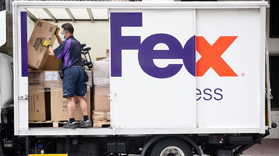 A FedEx worker gets packages from a truck