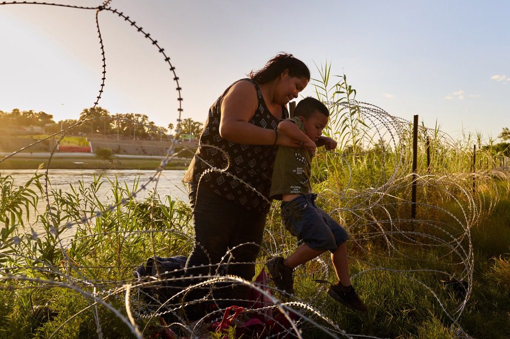 Portillo Alarcón, of Managua, Nicaragua, lifts her son Louise, 5, on barbed wire after crossing the US-Mexico border at the Rio Grande on Saturday, July 23, 2022 in Eagle Pass, Texas. 