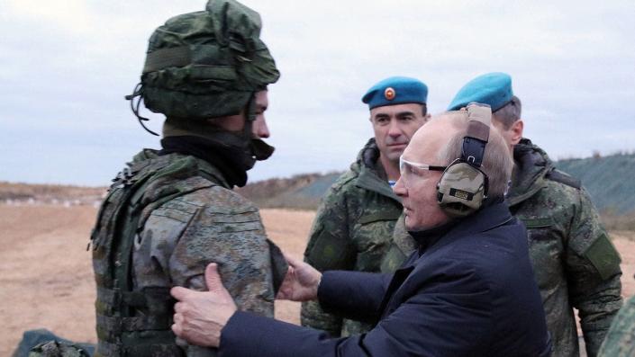 Putin wears a protective ear and an eye while talking to the soldier